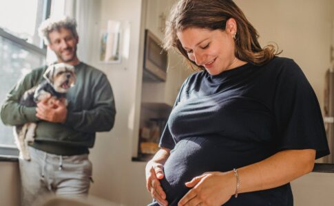 cheerful pregnant woman feeling child moving while husband with dog standing near