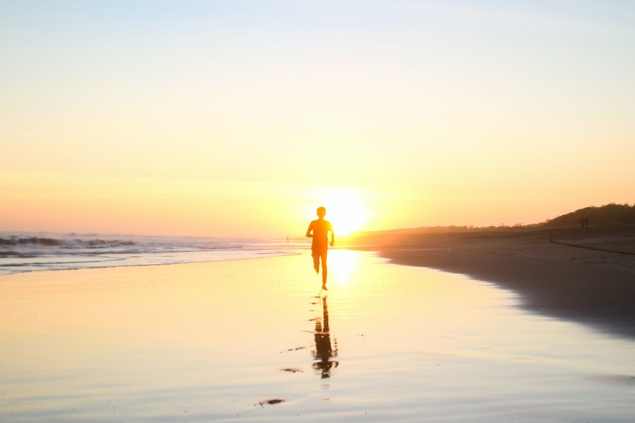 silhouette of boy running in body of water during sunset